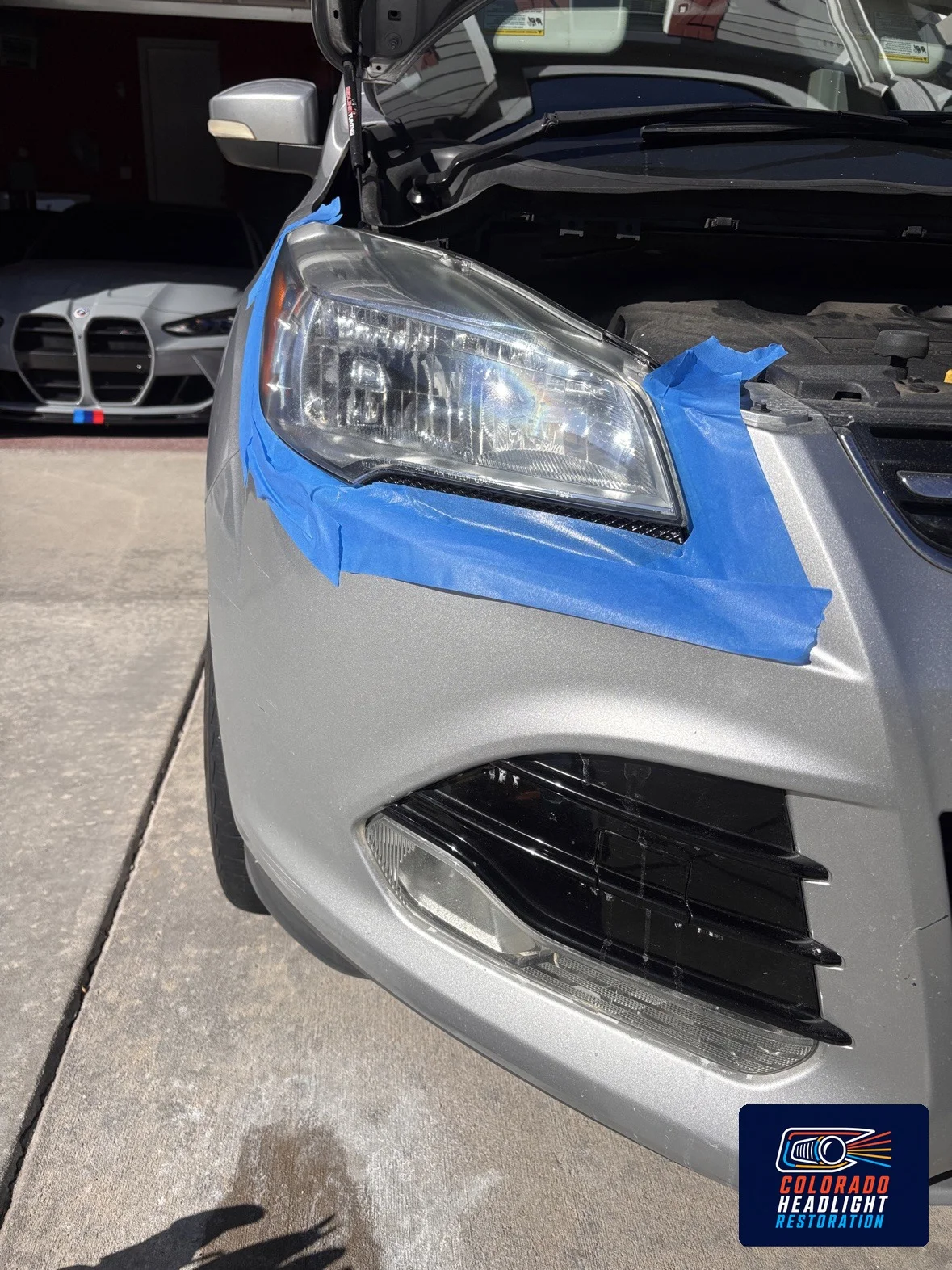 Silver car headlight with blue tape protecting surrounding paint