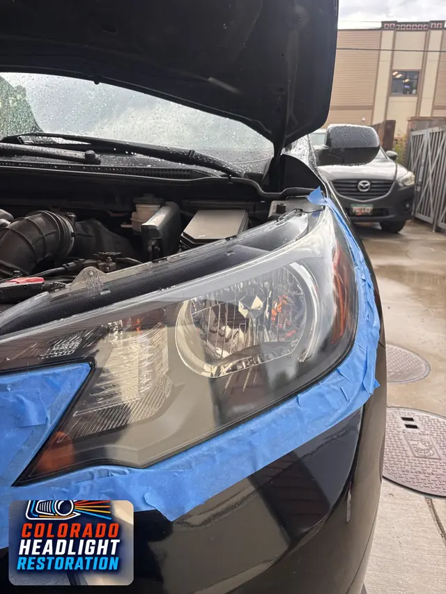Gray car headlight lens with blue tape protecting surrounding paint