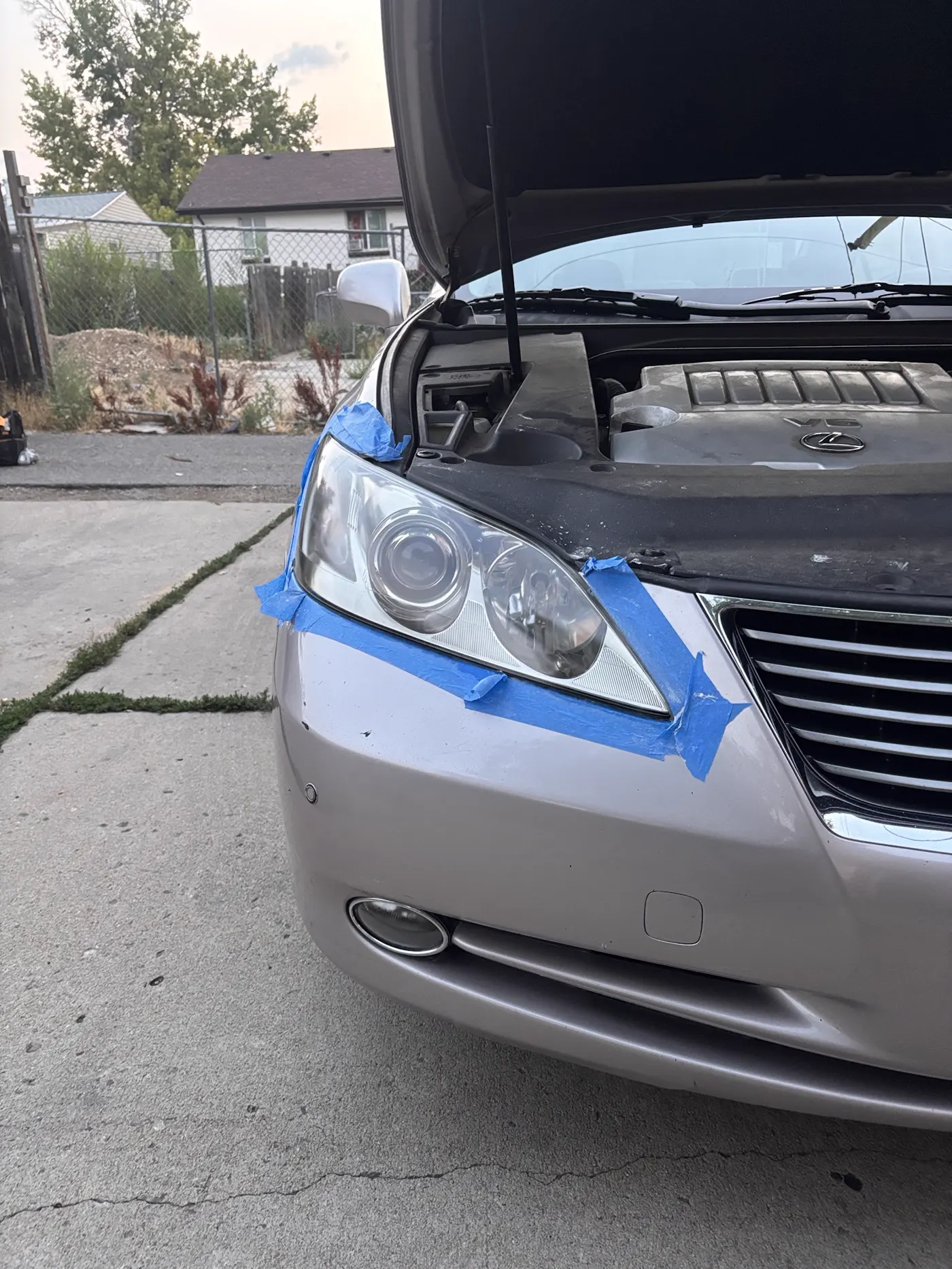 Silver sedan headlight with blue protective masking tape