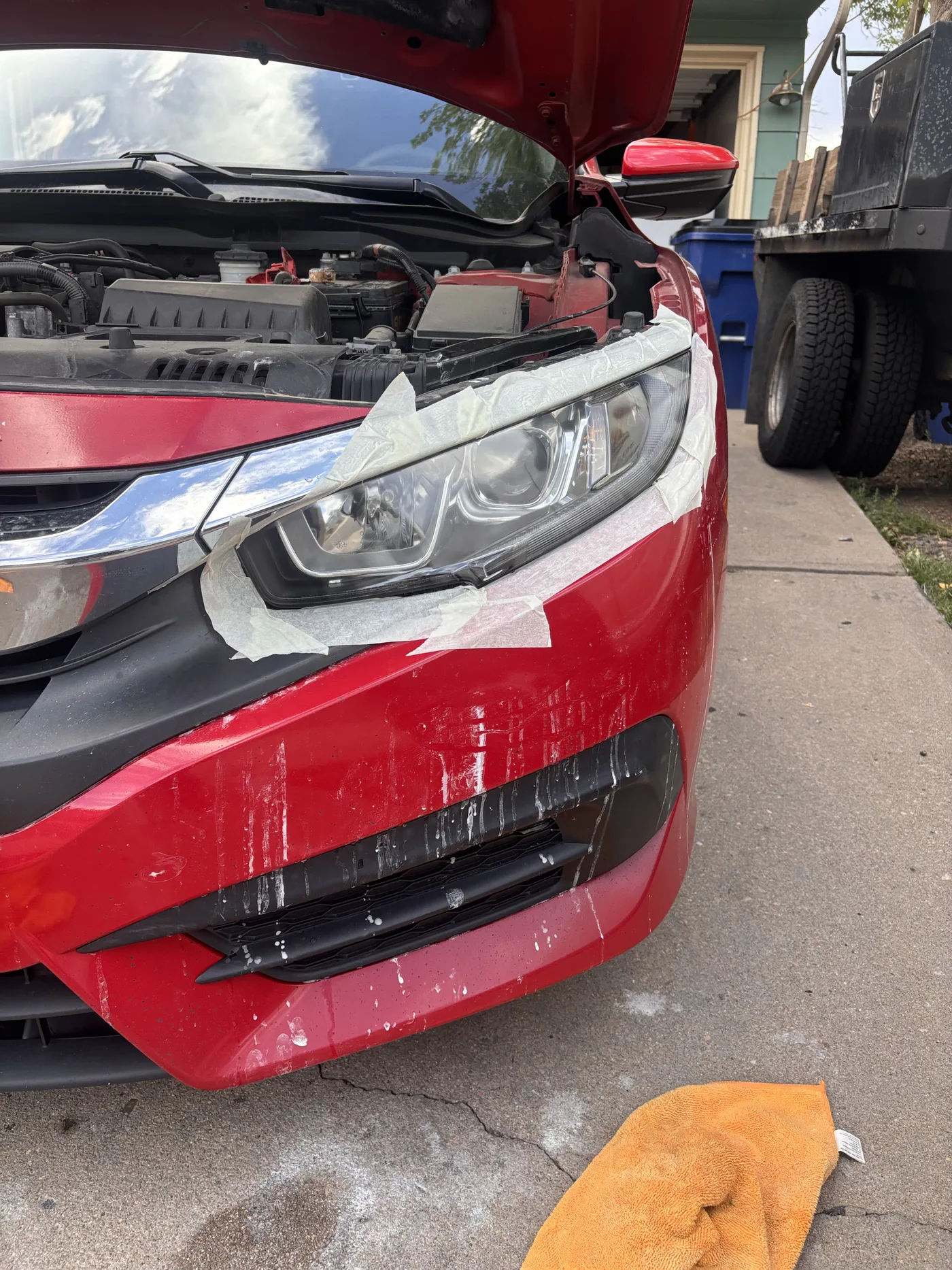 Red sedan headlight with blue tape protecting surrounding paint